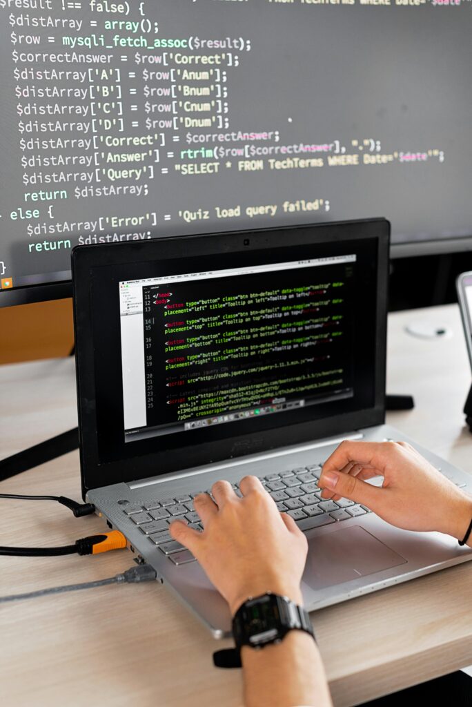 pexels photo 7988086 7988086 Person coding at a desk with laptop and external monitor showing programming code.
